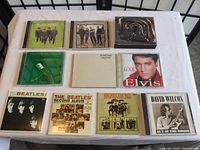 Photo showing 10 collectible CDs including 3 Beatles albums (The Beatles!, The Beatles' Second Album, Beatles '65), a double Rolling Stones set, Weezer, Pearl Jam album, Elvis Presley Love, Mannheim Steamroller Celebration, and David Wilcox Out of the Woods.
