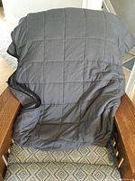 Dark gray weighted blanket draped over a chair showing square quilted stitch pattern and soft fabric texture.