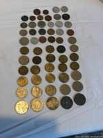Full view of 58 assorted European coins laid out in seven rows on cloth, showing various sizes, metals, and designs.
