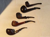 Five used tobacco pipes arranged on a white surface showing varying shapes, sizes, and colors.