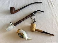 Overview photo showing four used tobacco pipes on a cloth surface, showcasing their size and design variety.