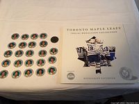 All 24 Toronto Maple Leafs medallions arranged on a white surface beside the official booklet for the 2002-03 medallion collection by Toronto Sun.