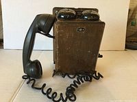 Front view of Northern Electric Model 717 wood box wall mount magneto telephone with handset attached by coiled cord.
