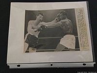 Black and white photo showing Rocky Graziano punching Sugar Ray Robinson in boxing ring with caption attached on right side.