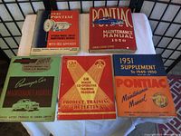 Photo showing five vintage vehicle manuals arranged on a table with covers visible, including Pontiac and GM models with years from early 1950s