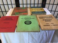Lot of 4 vintage vehicle maintenance manuals on a white cloth background.