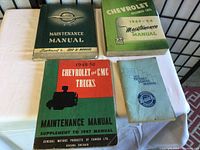 Four vintage vehicle maintenance manuals laid out on a white fabric surface, showing covers with titles and years.