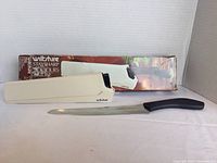 Photo showing the cutting utensil, holder, and distressed original packaging.