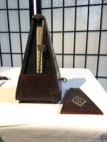 Frontal view of vintage Wittner mechanical metronome with the top cover removed and placed beside it, showing the pendulum scale and wooden base with minor wear and repaired bottom front.