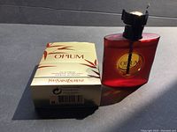 Yves Saint Laurent Opium 50ml spray bottle and original box side by side under light showing bottle color and box design.