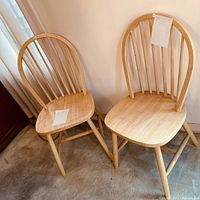 Two natural wood chairs with spindle backs, light wood finish, placed on carpet near curtain and cabinet.