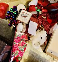 Photo showing the Christmas bear lying among various holiday decorations including a wreath, pillow, CD, Santa hat, and glitter bow
