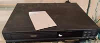 Black JVC VHS player with front tray and control buttons visible on front panel, used condition with some surface scratches