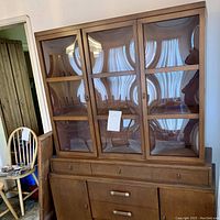 Front view of mid-century wooden buffet with beveled glass doors and drawers.