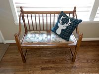 Front view of wood bench with upholstered double seats and plaid decorative pillow with deer silhouette.