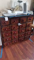 View of wooden cabinet with four small drawers on top and two cabinet doors below; sewing machine placed on top; cabinet has visible wear.