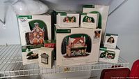 Shelf view showing two large green and white Department 56 building boxes and assorted smaller accessory boxes