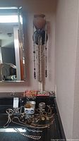 View of jewelry displayed on counter including bracelets, rings, pins, and a tin box with lid. Necklaces hanging on wall sconce above.
