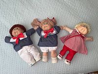 Front view of three Cabbage Patch Kids dolls lying on a light blue surface.