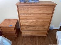Photo of 5 drawer oak dresser and 2 drawer oak night stand side by side on wood floor near a wall.