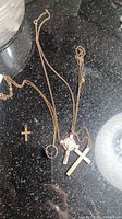 Photo of 3 gold crucifix pendants, two on chains and one loose, plus a ring on a chain, displayed on black marble surface.
