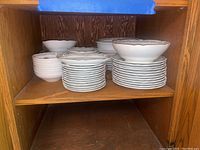 Wooden shelving holding stacks of dishes including bowls and plates with green and gold rim Noritake pattern
