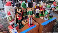 Group photo showing nine nutcrackers lined up on a table from 11 to 17 inches tall, including human and animal figures in colorful outfits.