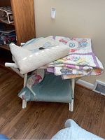 White folding wooden luggage rack holding three folded quilts.