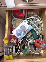 Drawer with various rolls of tape, extension cords, measuring tape, and two GE decorative light bulbs in packaging