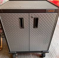 Front view of Gladiator tool cabinet showing diamond plate front doors with recessed handles and lock on right door, caster wheels at the base.