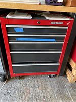 Front view of red and black Craftsman tool cabinet with five drawers, a lock on the top drawer, caster wheels visible at bottom, with some wear and minor scratches on the frame.