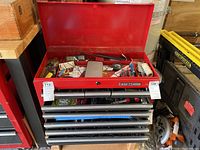 Front view of the open Craftsman tool cabinet showing the red metal top lid open revealing storage area with assorted items (items not included). 7 drawers below lid visible.