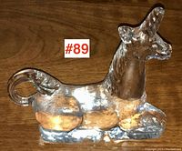 Front side view of clear Kosta Boda glass unicorn, showing curled tail and elongated horn.