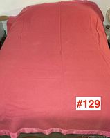 Full view of the pink wool blanket spread on a bed, showing solid pink color and the edge trim.