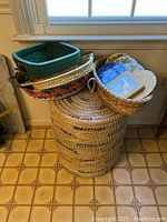 Photo showing the baskets stacked with assorted trivets placed on top and inside some baskets near a window.