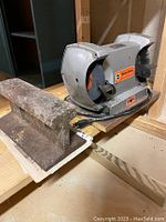 Photo of used Black & Decker bench grinder with two grinding wheels and attached brush, sitting on a wooden surface next to a large anvil or metal block.