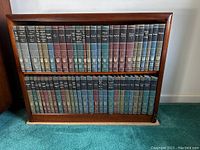 Two shelves of a wooden bookcase containing a complete set of 54 Britannica Great Books volumes, numbered 1 to 54, in assorted colors with gold lettering and decorative designs on the spine.