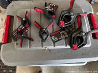 Photo showing seven assorted spring clamps in black and red, some are 3-inch and others 6-inch sizes. Several have brand tags from Tekton.