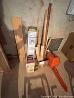 Photo showing various pieces of miscellaneous lumber, Frost King plastic sheeting box, and orange Stihl chainsaw case.