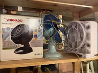 Photo showing all three fans on a wooden shelf, including the boxed Vornado fan, vintage Westinghouse fan, and small white fan.
