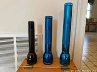 Three flashlights of different sizes and colors arranged upright on a wooden surface without chest visible.