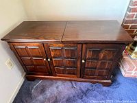 Front view of dark wooden flip-top server with three paneled doors and brass knobs.