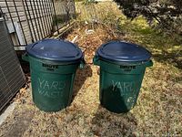 Photo showing two green Rubbermaid Brute garbage cans with lids placed outdoors, labeled 'YARD WASTE'.