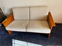 Full front view of the love seat showing the tan cushions on a wooden frame.