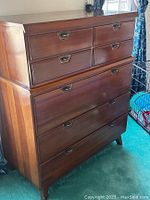 Oblique angled view of midcentury modern wood chest of drawers showing side and front with six drawers and recessed metal handles.