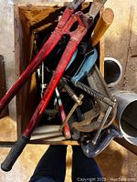 Photo showing a top view inside one wooden box filled with various tools including large red bolt cutters, C-clamps, hacksaw, pipe wrench and files.