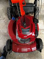 Top-front view showing red Toro Vortex mower engine cover, pull cord, handle and wheels
