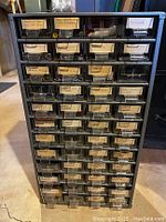 Front view of PowerKraft hardware chest with multiple labeled plastic drawers containing assorted hardware parts including screws, bolts, nails, and grommets.