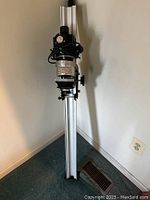 Photo of Simmon Omega B22 enlarger standing vertically showing aluminum column and black head with cord wrapped around it.