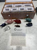 Set of seven elephant figurines in various colors displayed in front of a padded, compartmented carrying case, along with an informational card from the Smithsonian Institution.